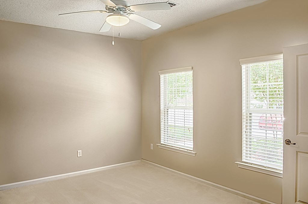 A room with a ceiling fan and two windows with blinds.