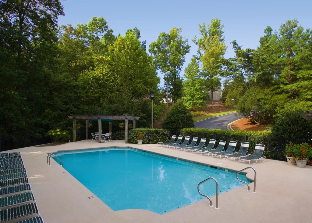 A pool surrounded by trees and chairs.