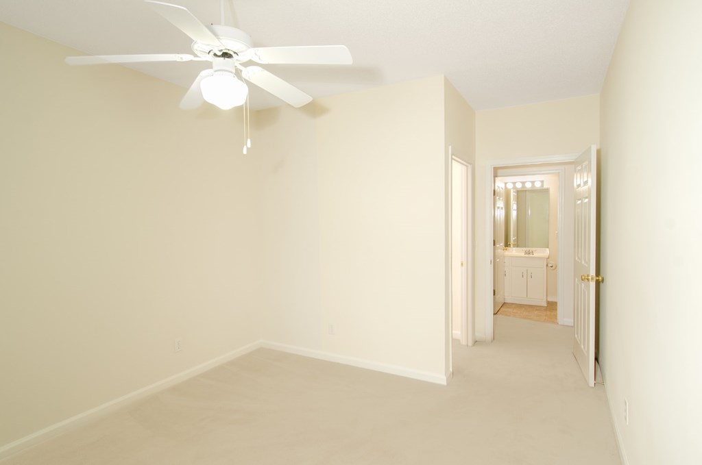 A white room with a ceiling fan and a doorway leading to another room.