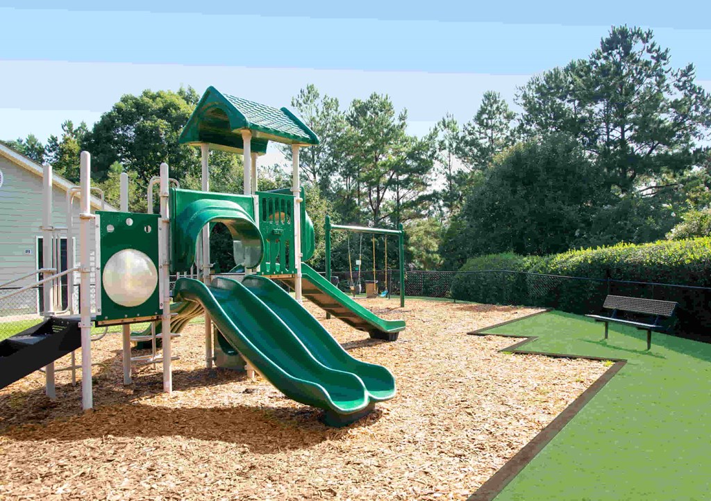 A playground with a green slide and a wooden structure.