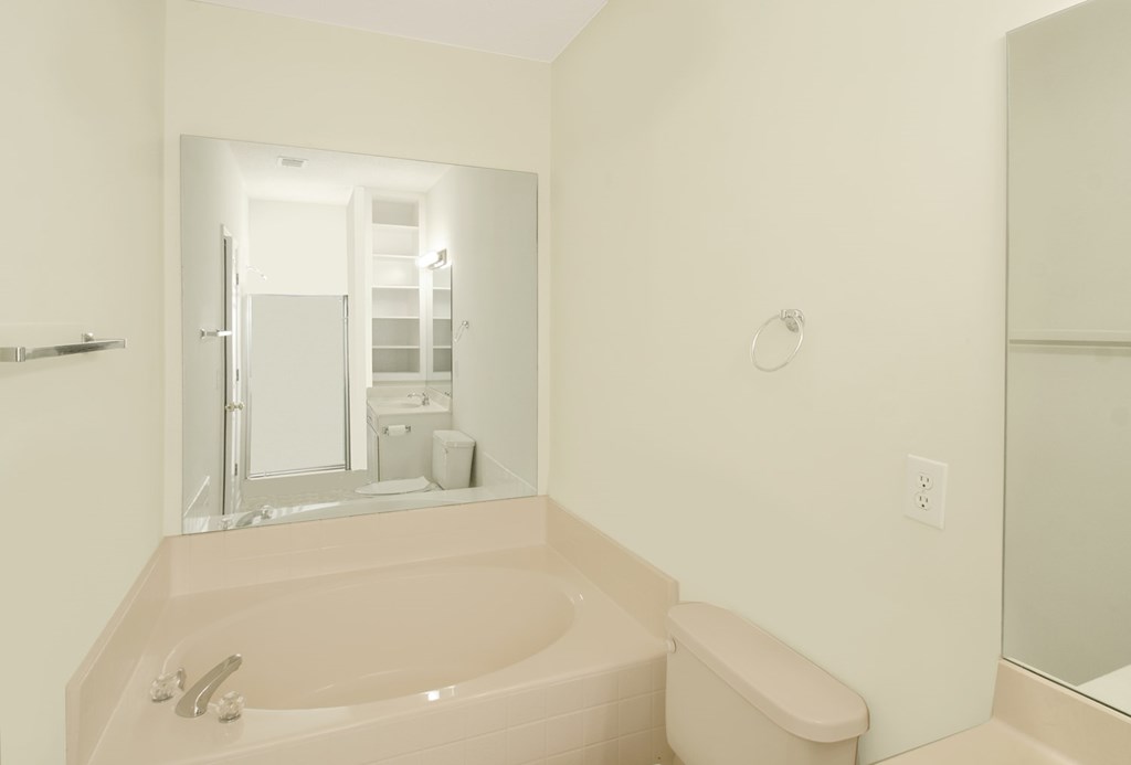 A white bathroom with a tub and a mirror.