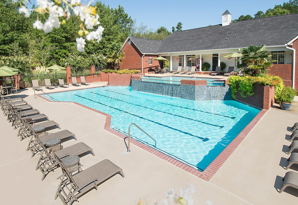 A large swimming pool surrounded by lounge chairs and a house in the background.