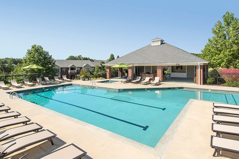 A large swimming pool with sun loungers and a pavilion in the background.