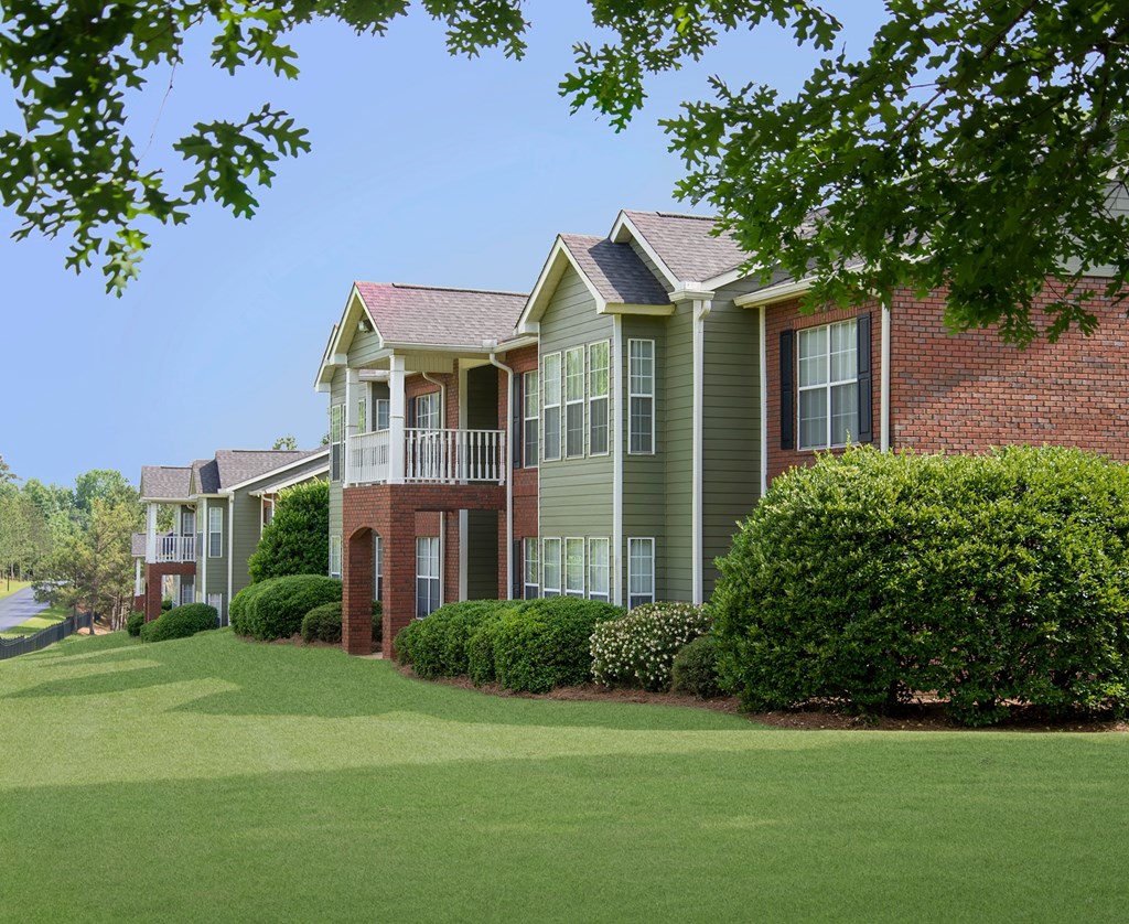 A row of houses with green lawns and trees in front.