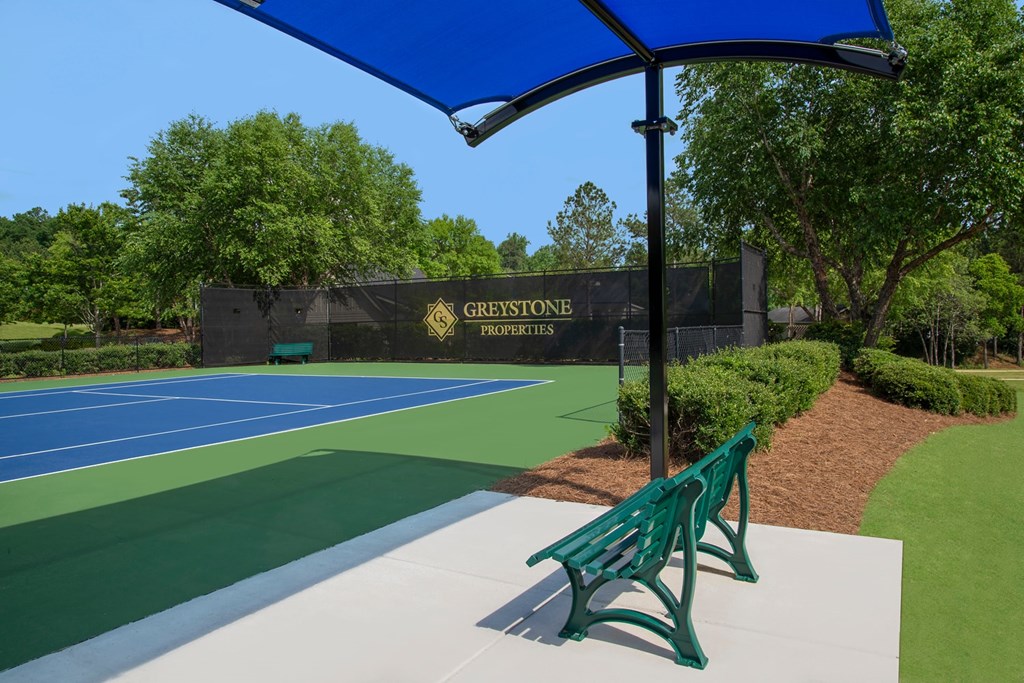 A tennis court with a blue umbrella and a sign that says "Greystone Properties".