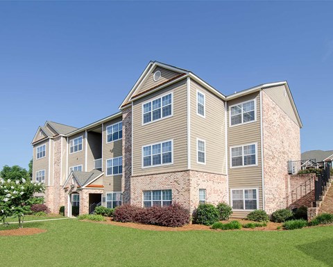 A large, multi-story residential building with a brick facade and a green lawn in front.