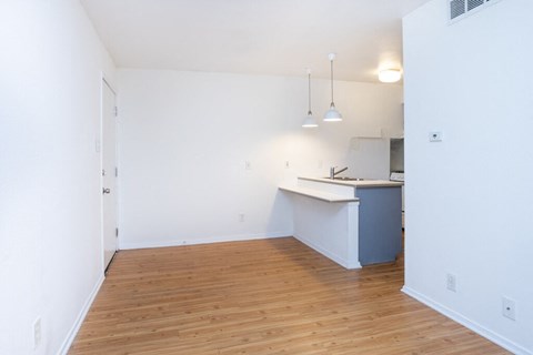 an empty living room and kitchen with wood floors and white walls