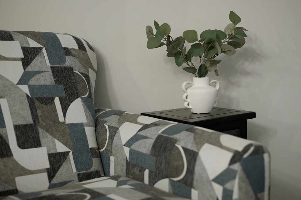 A grey and white patterned sofa with a white vase on a small table.