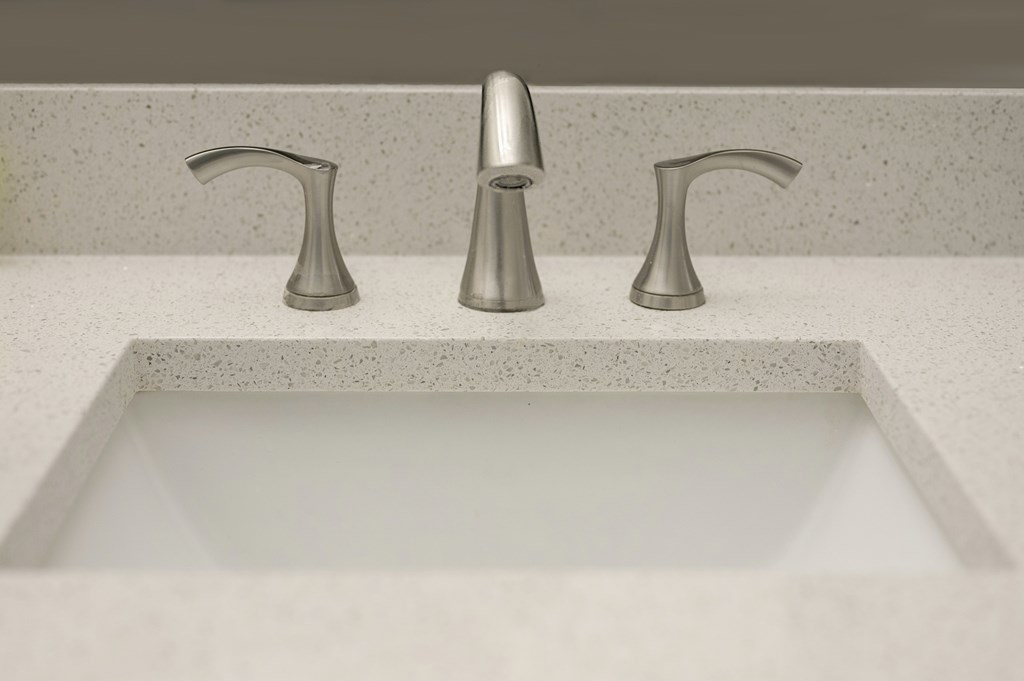 Three metallic faucets are mounted on a white sink.