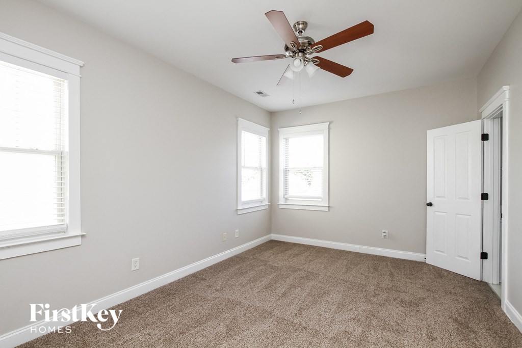 A room with a carpet floor, a ceiling fan, and a door.