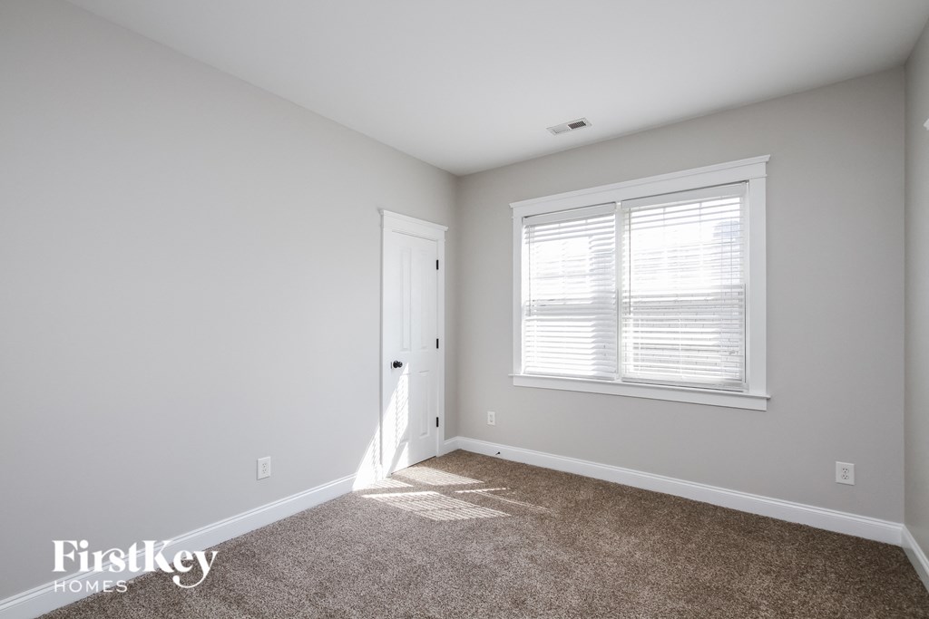 A room with a carpeted floor, a window with blinds, and a door.