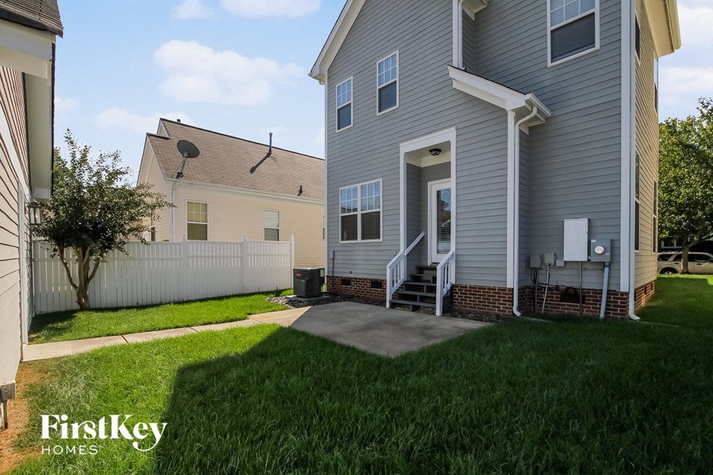 A grey house with a white fence and a tree in the front yard.
