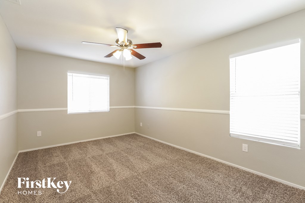 a carpeted room with a ceiling fan and two windows