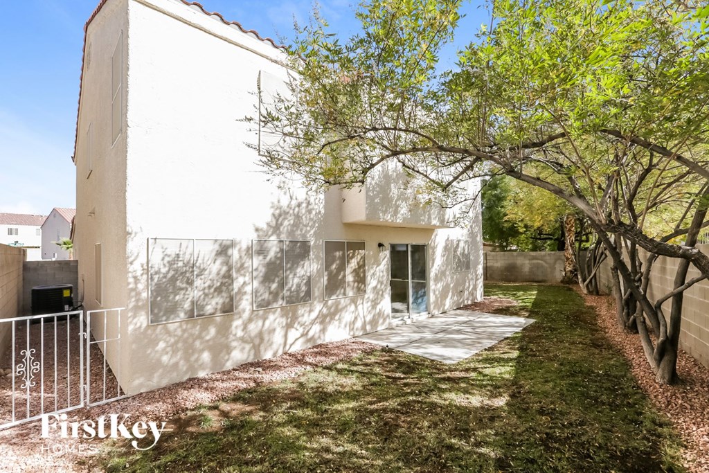 the side of a house with a sidewalk and trees