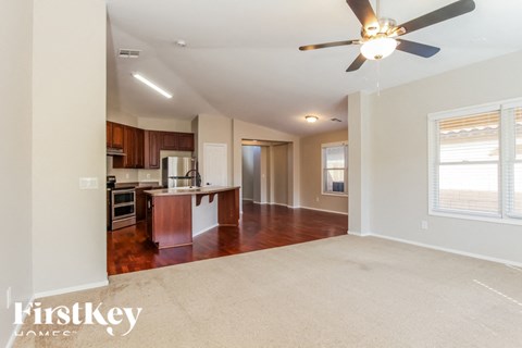 A spacious living room with a kitchen in the background and a carpet on the floor.