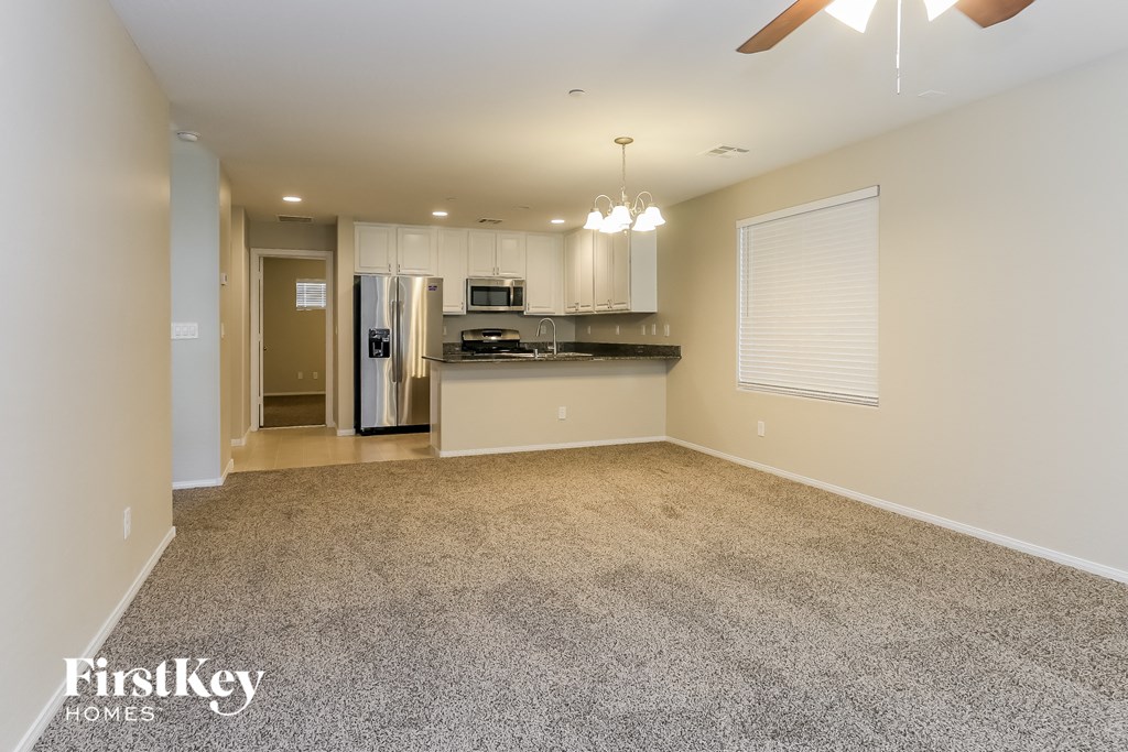 an empty living room with a kitchen and a ceiling fan