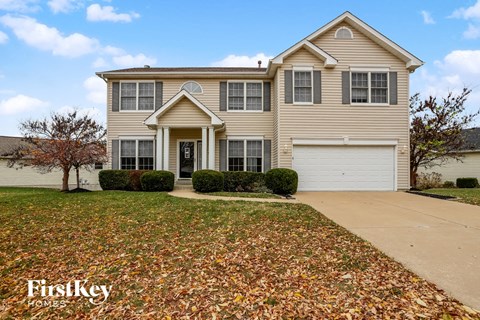 A house with a driveway and a tree with leaves on the ground.