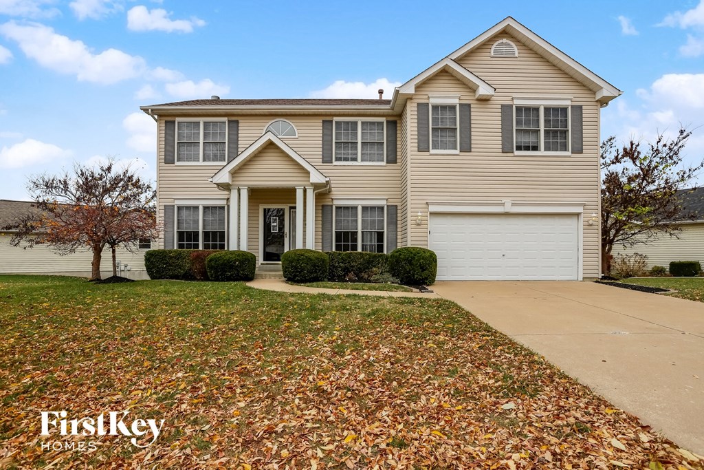 A house with a driveway and a tree with leaves on the ground.