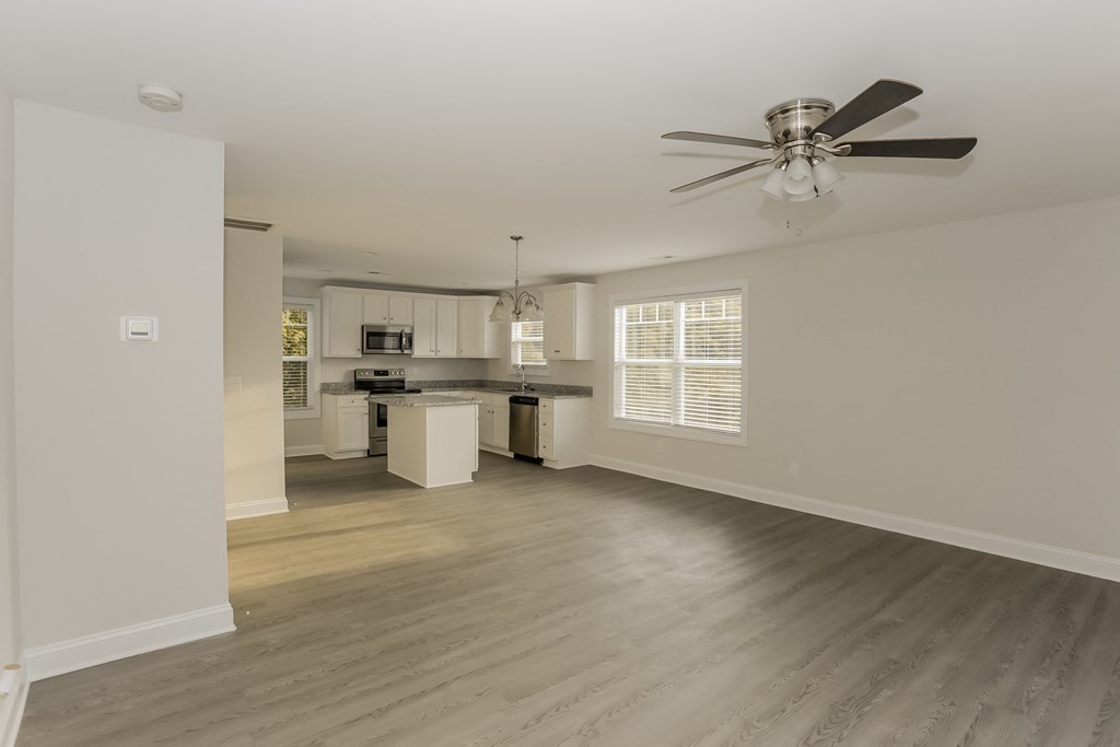 an empty living room with a ceiling fan and a kitchen