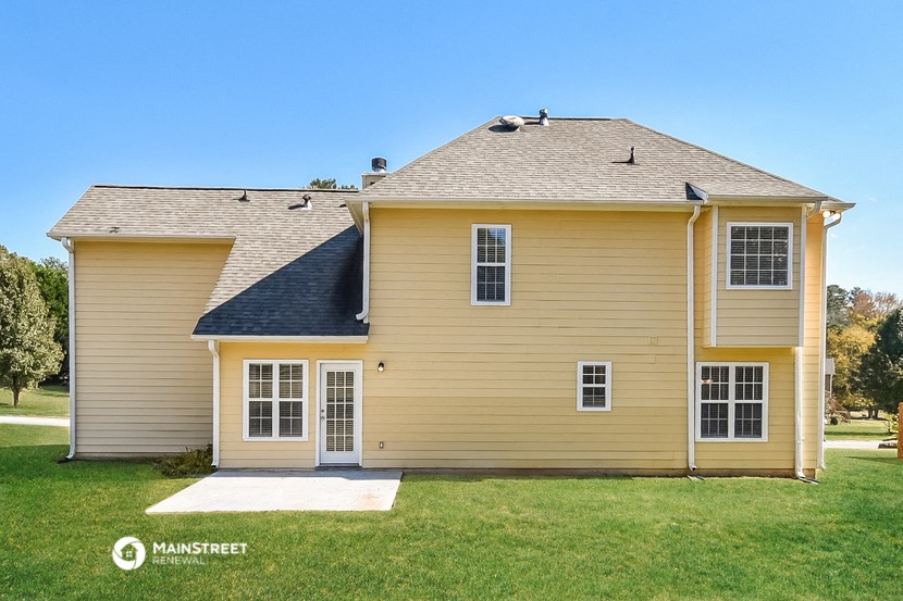 a yellow house with a gray roof on a grass field