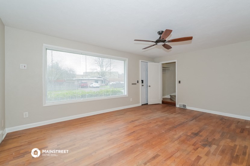 an empty living room with a large window and a ceiling fan