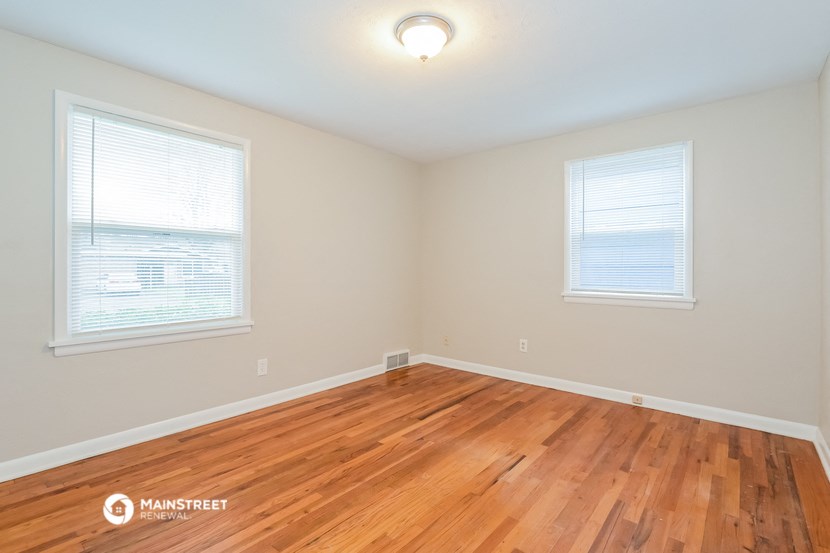 the spacious living room with hardwood floors and two windows