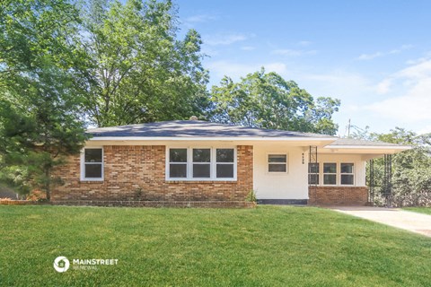 a small brick house with a lawn and trees