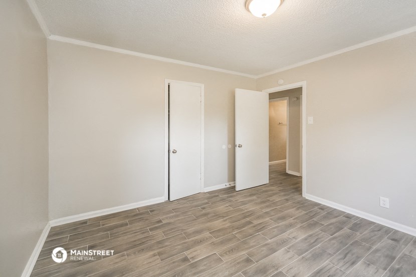 the living room of an apartment with white walls and wood flooring