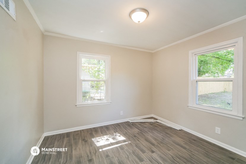 the interior of an empty room with wood flooring and two windows