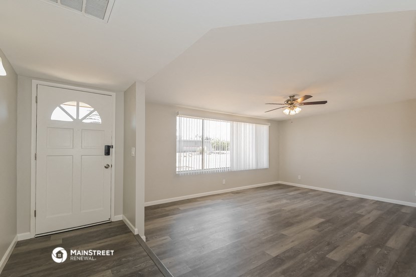 the spacious living room with a white door and ceiling fan
