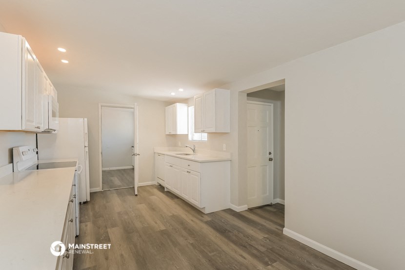 a renovated kitchen with white cabinets and white appliances and wood flooring