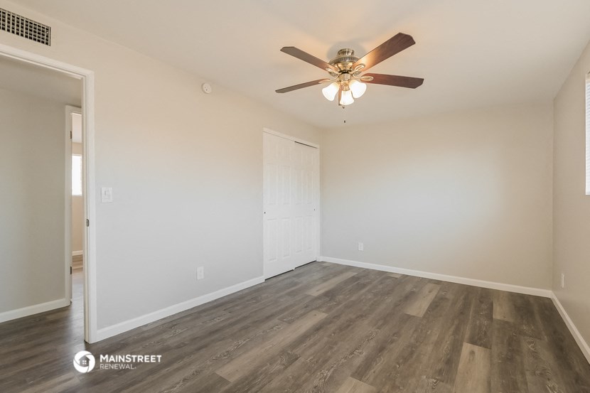 the spacious living room with wood flooring and a ceiling fan