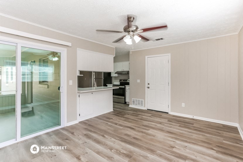 an empty living room with a ceiling fan and a kitchen