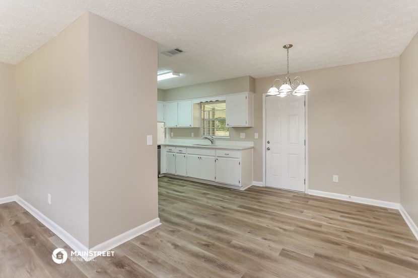 an empty living room and kitchen with wood flooring and white cabinets