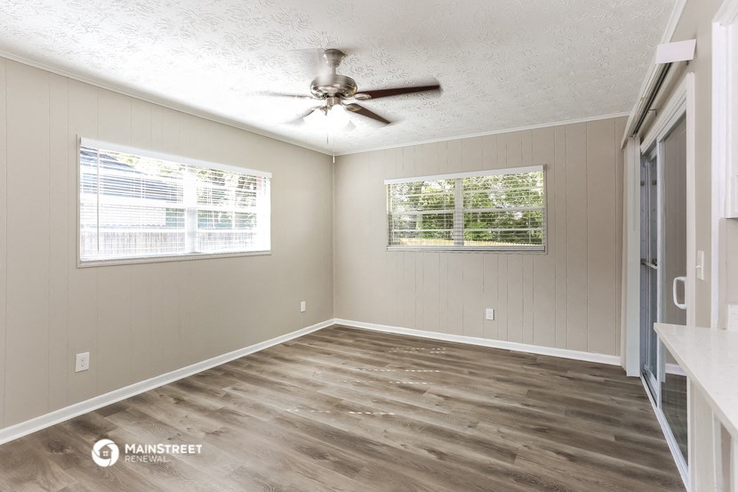 an empty living room with a ceiling fan and two windows