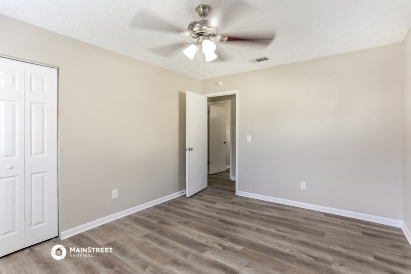 the spacious living room with ceiling fan and door to the hallway