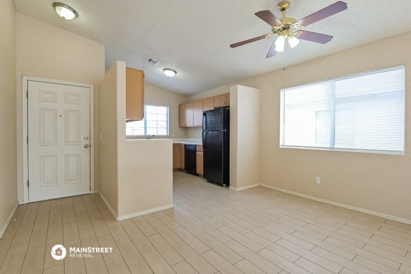 an empty living room with a kitchen and a ceiling fan