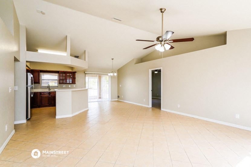an empty living room with a ceiling fan and a kitchen