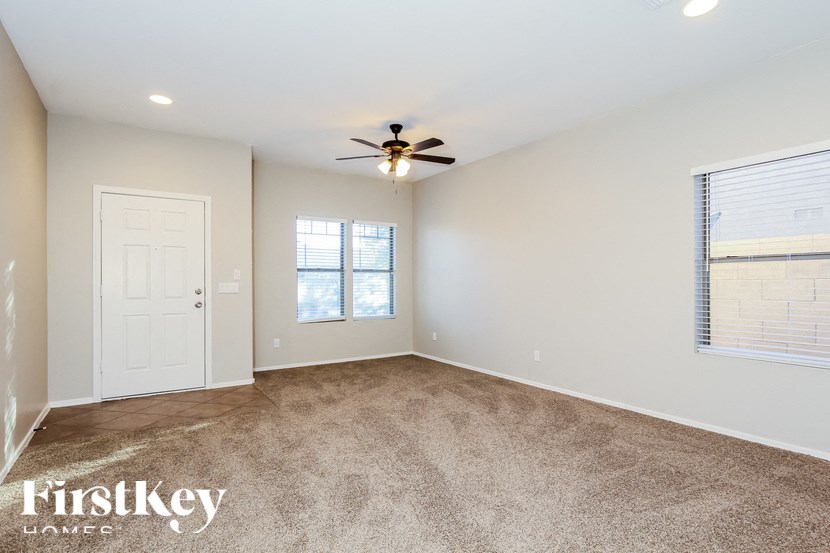 A spacious room with a carpeted floor, a ceiling fan, and a door leading to another room.