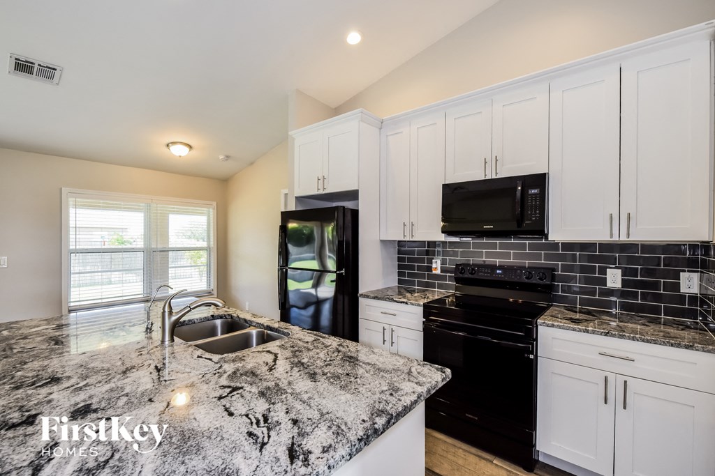 a kitchen with white cabinets and black appliances and granite counter tops