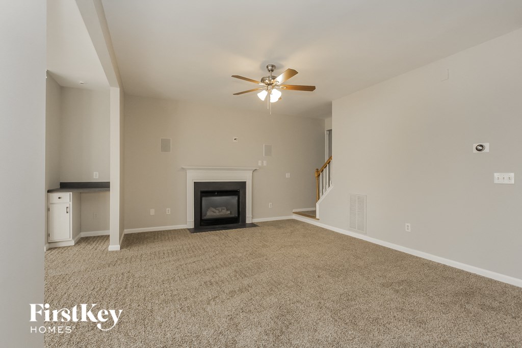 an empty living room with a fireplace and a ceiling fan