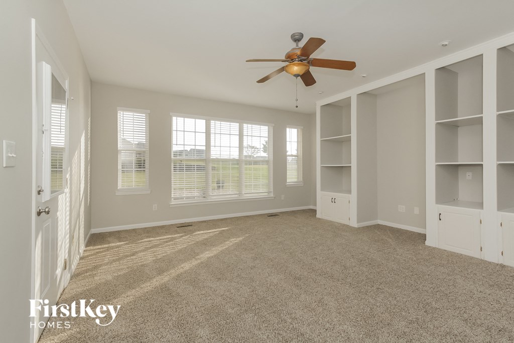 an empty living room with a ceiling fan and white shelves