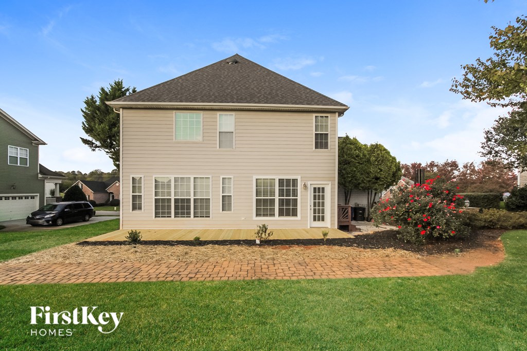 a yellow house with a brick walkway in front of a lawn and a tree