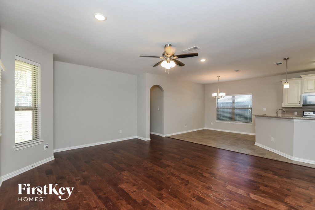 an empty living room with a ceiling fan and a kitchen