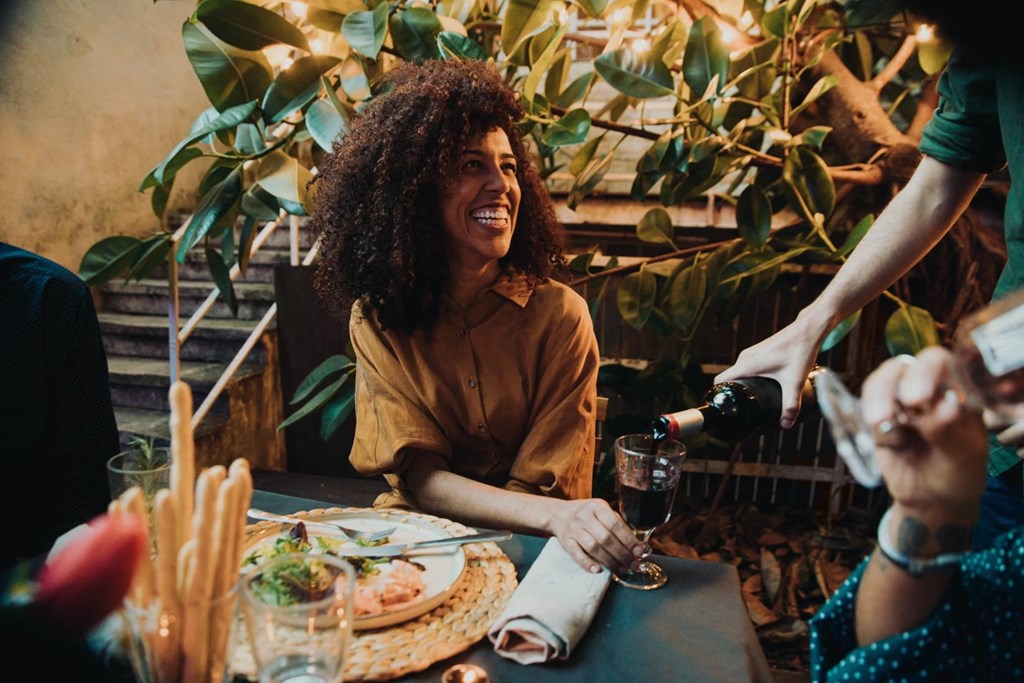 a woman sitting at a table with a plate of food and a glass of wine