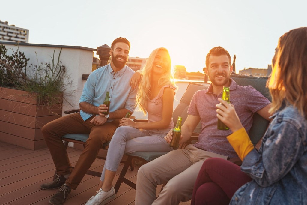 a group of people sitting on a roof terrace holding beers