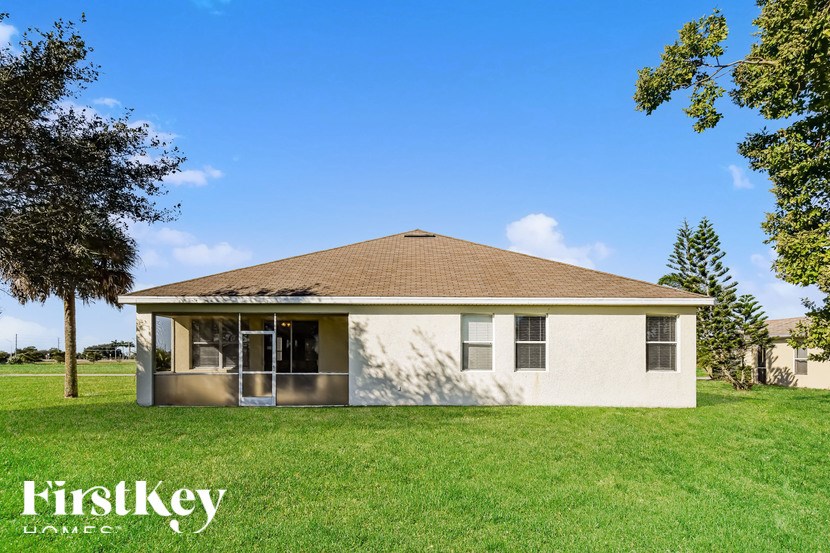 A house with a brown roof and a white exterior is surrounded by green grass and trees.