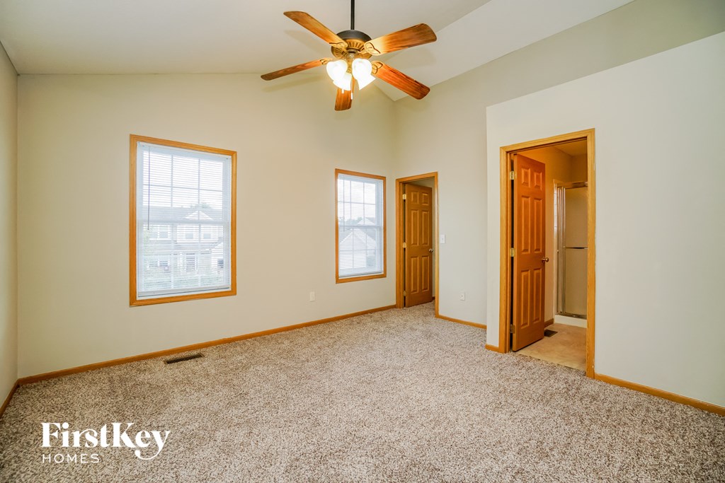 A room with a carpet floor, a ceiling fan, and three windows.