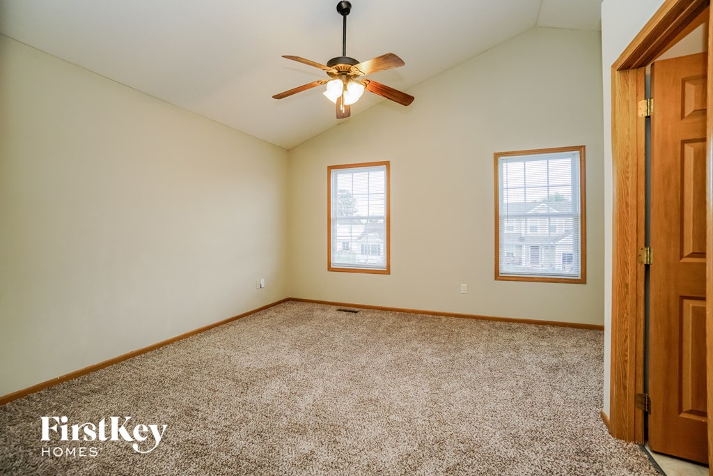 A room with a carpeted floor, a ceiling fan, and two windows.