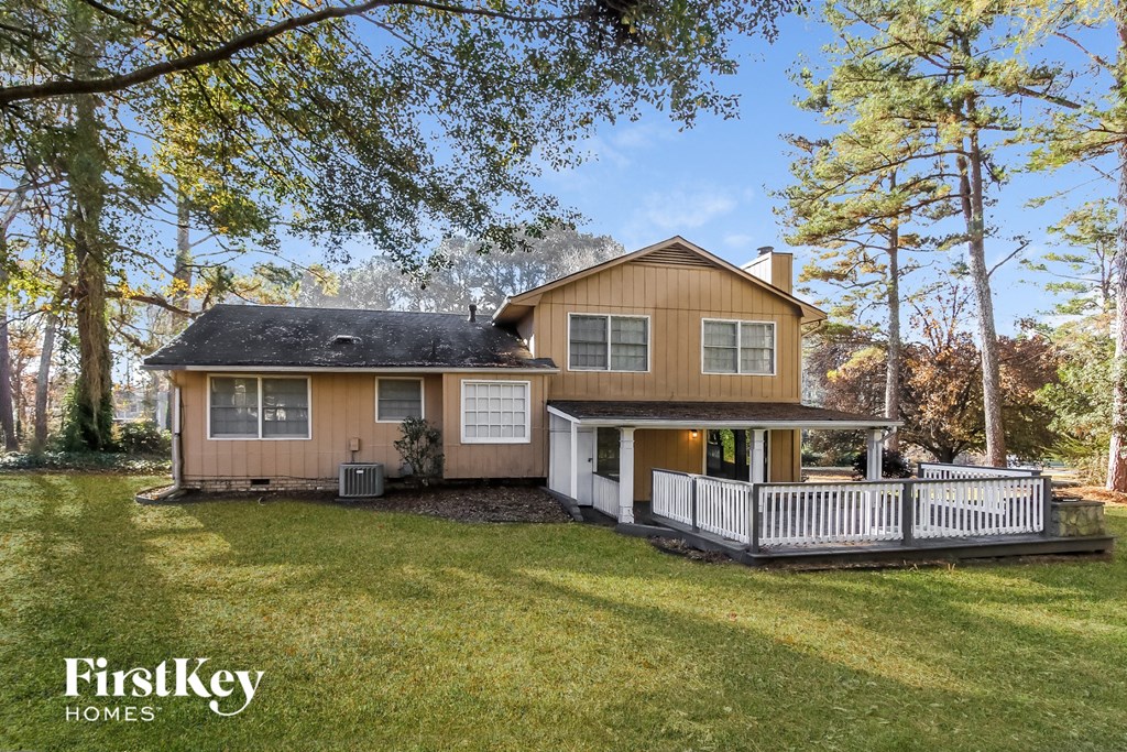 A house with a brown exterior and a black roof is surrounded by trees and has a white fence.